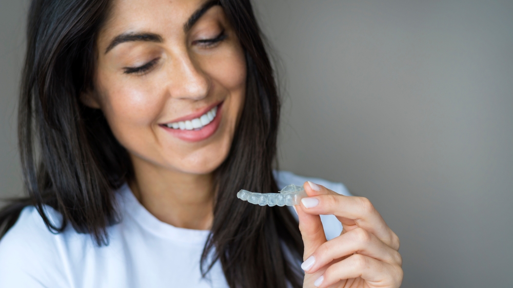 A smiling woman looking at SureSmile Clear Aligners, happy with her treatment from Renewal Family Dental.