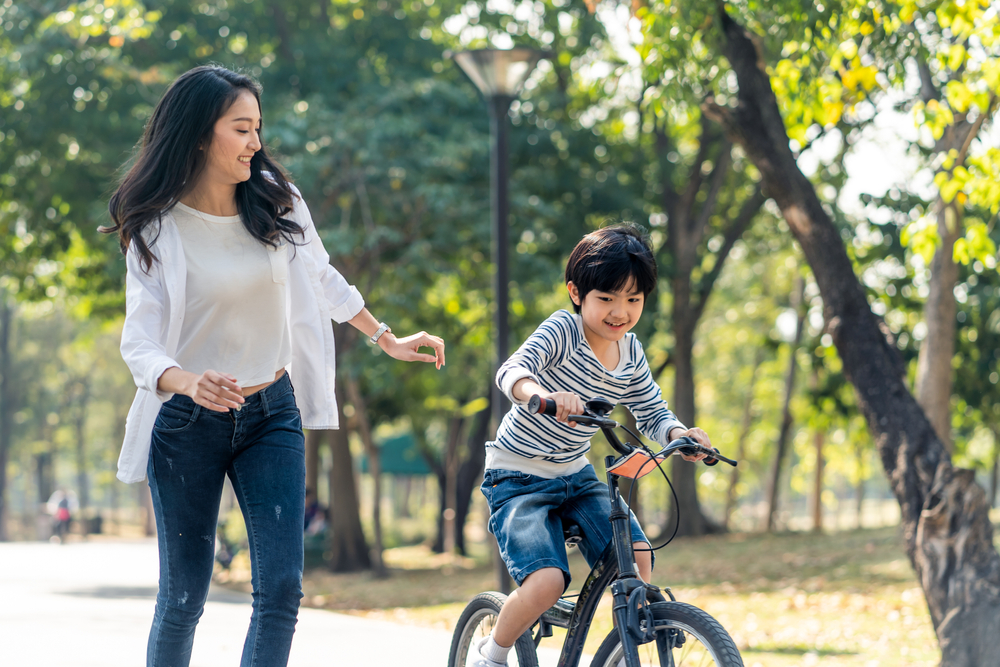 A smiling woman helping a joyful boy learn to ride a bike, reflecting the healthy, active families cared for by Renewal Family Dental.