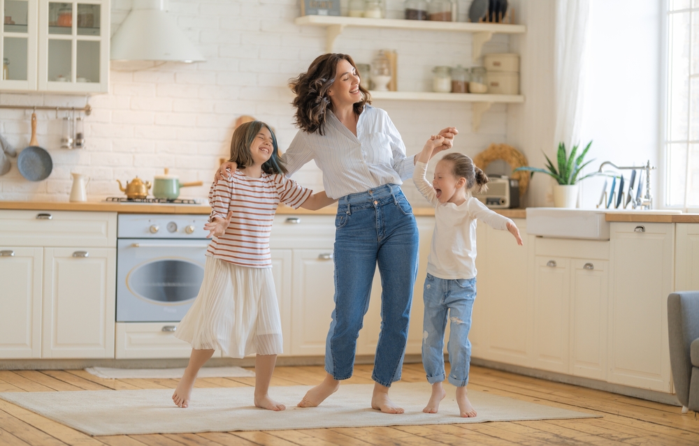 A joyful mother and two daughters dancing in a bright kitchen, reflecting the happy, healthy families Renewal Family Dental serves.
