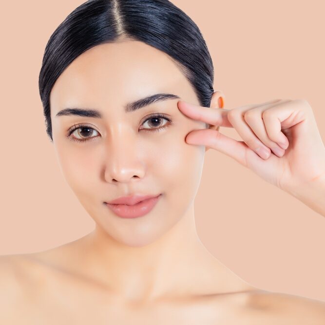 A smiling woman with clear skin, pulling at her eye, representing a refreshed look from Renewal Family Dental.