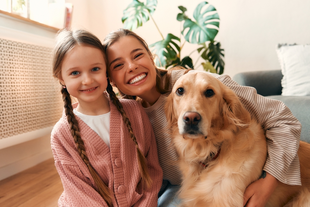 A smiling mother and daughter with their golden retriever, representing the warm, family-friendly atmosphere of Renewal Family Dental.
