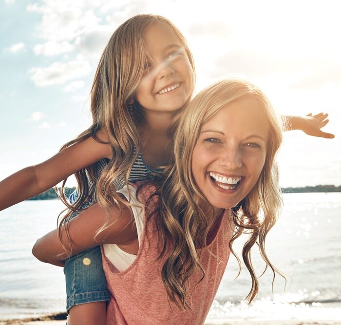 A joyful mother giving her daughter a piggyback ride on a sunny day, reflecting the happy families at Renewal Family Dental.