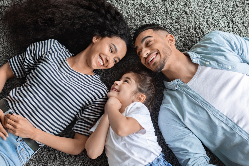 A joyful family lying on a rug, looking at each other and smiling, embodying the happy connections Renewal Family Dental fosters.
