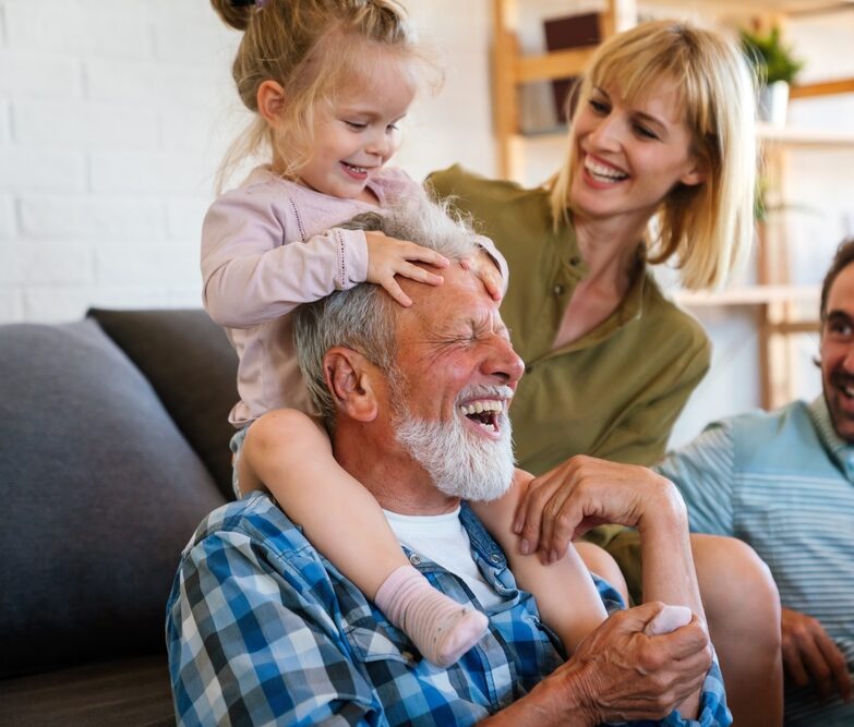 A joyful family laughing together, with a child on an older man's shoulders, embodying the warmth of Renewal Family Dental.