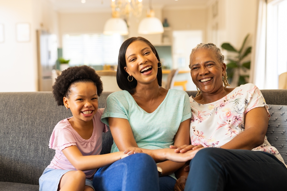 Three generations of women laughing happily on a couch, representing Family Dentistry in Dearborn at Renewal Family Dental.