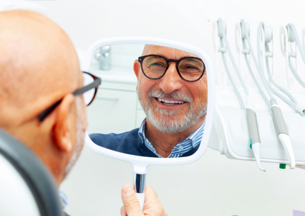 A smiling man looking in a mirror at his new teeth from Dental Implants in Dearborn at Renewal Family Dental.